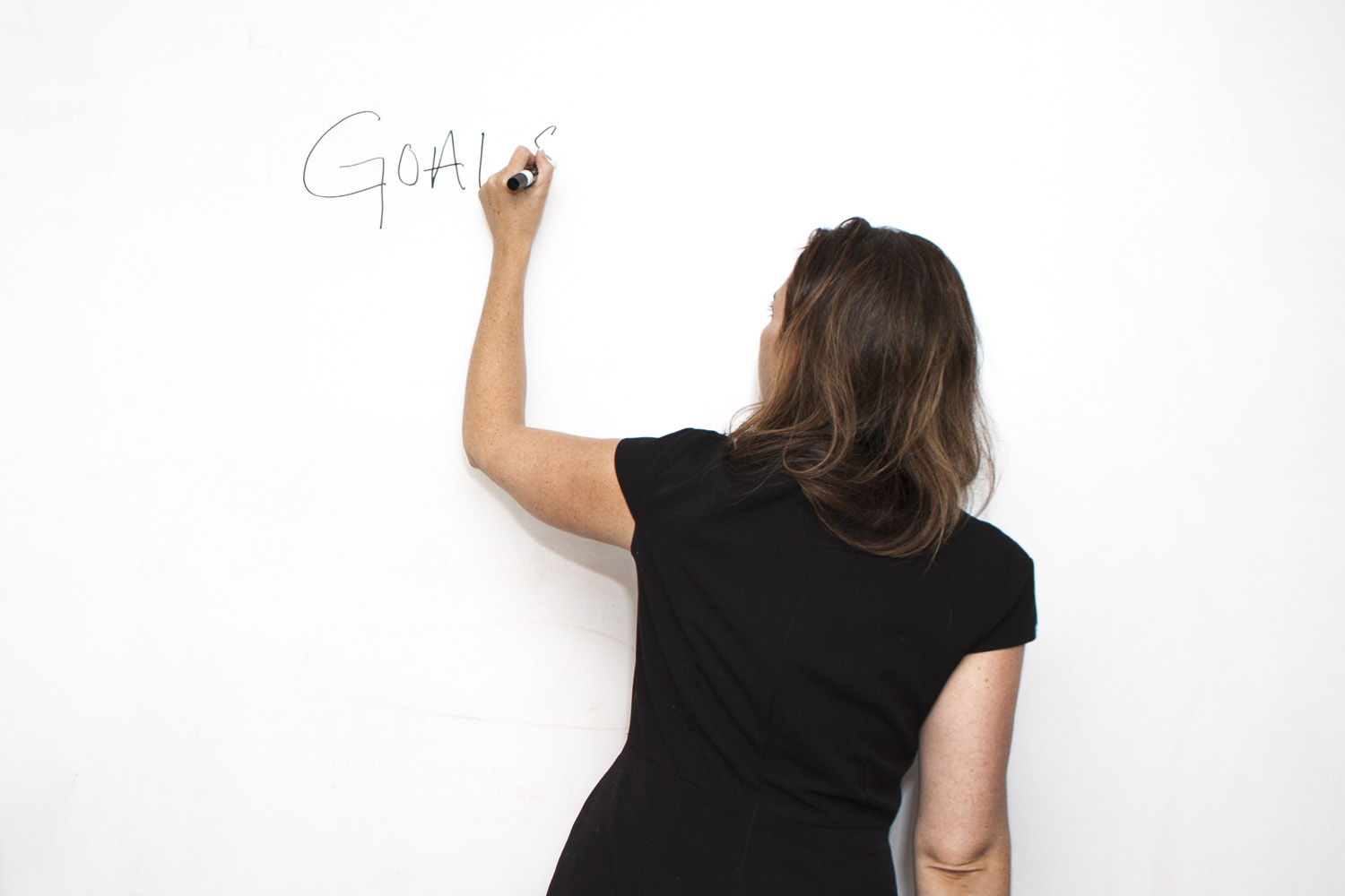 Trainer writing key concepts on a whiteboard during a workshop. The trainer, dressed in business casual attire, is using a marker to draw diagrams or jot down important points.