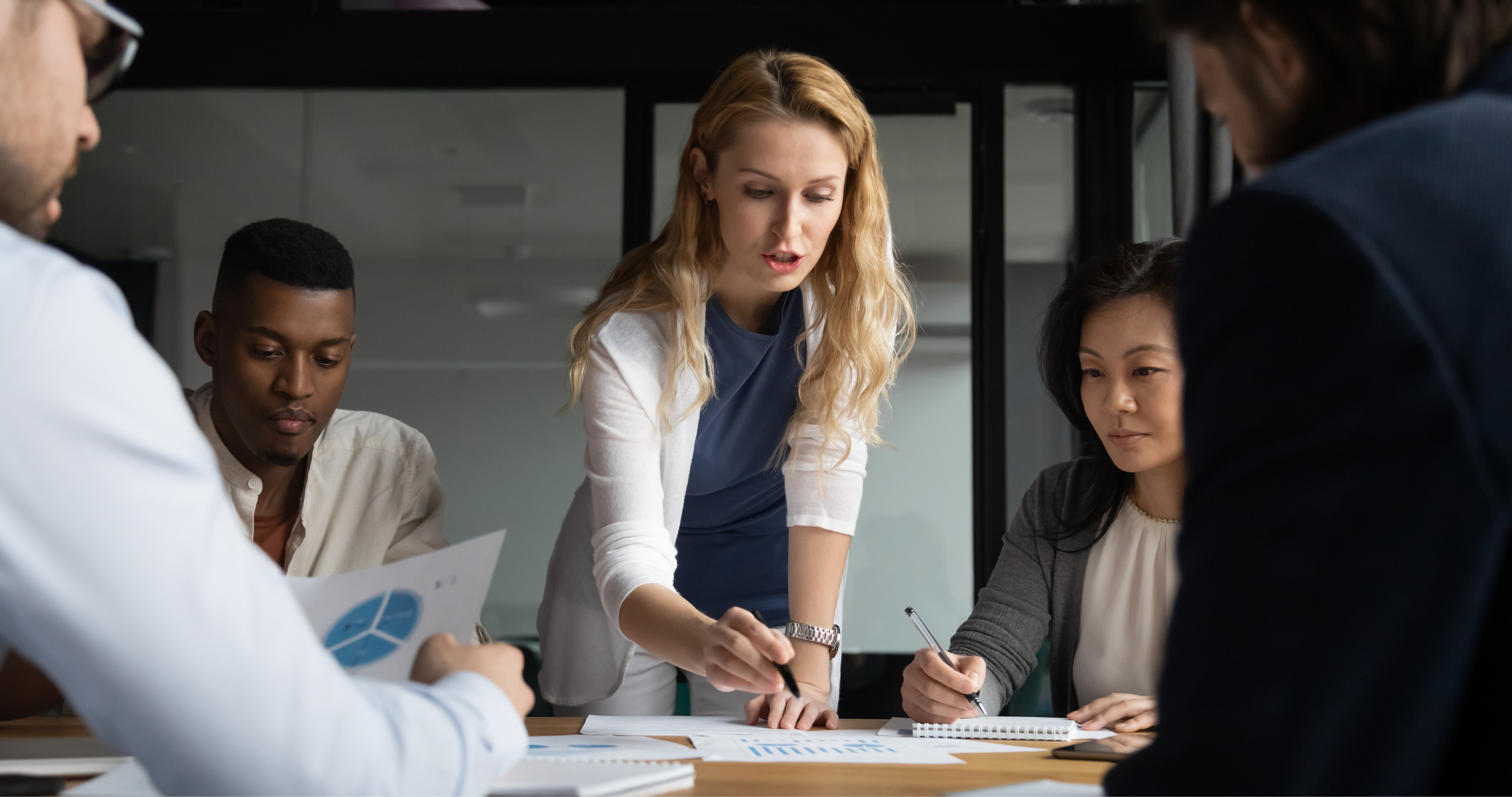 A woman with her team, holding a pen and about to write on a large piece of paper during a Key Account Management session.