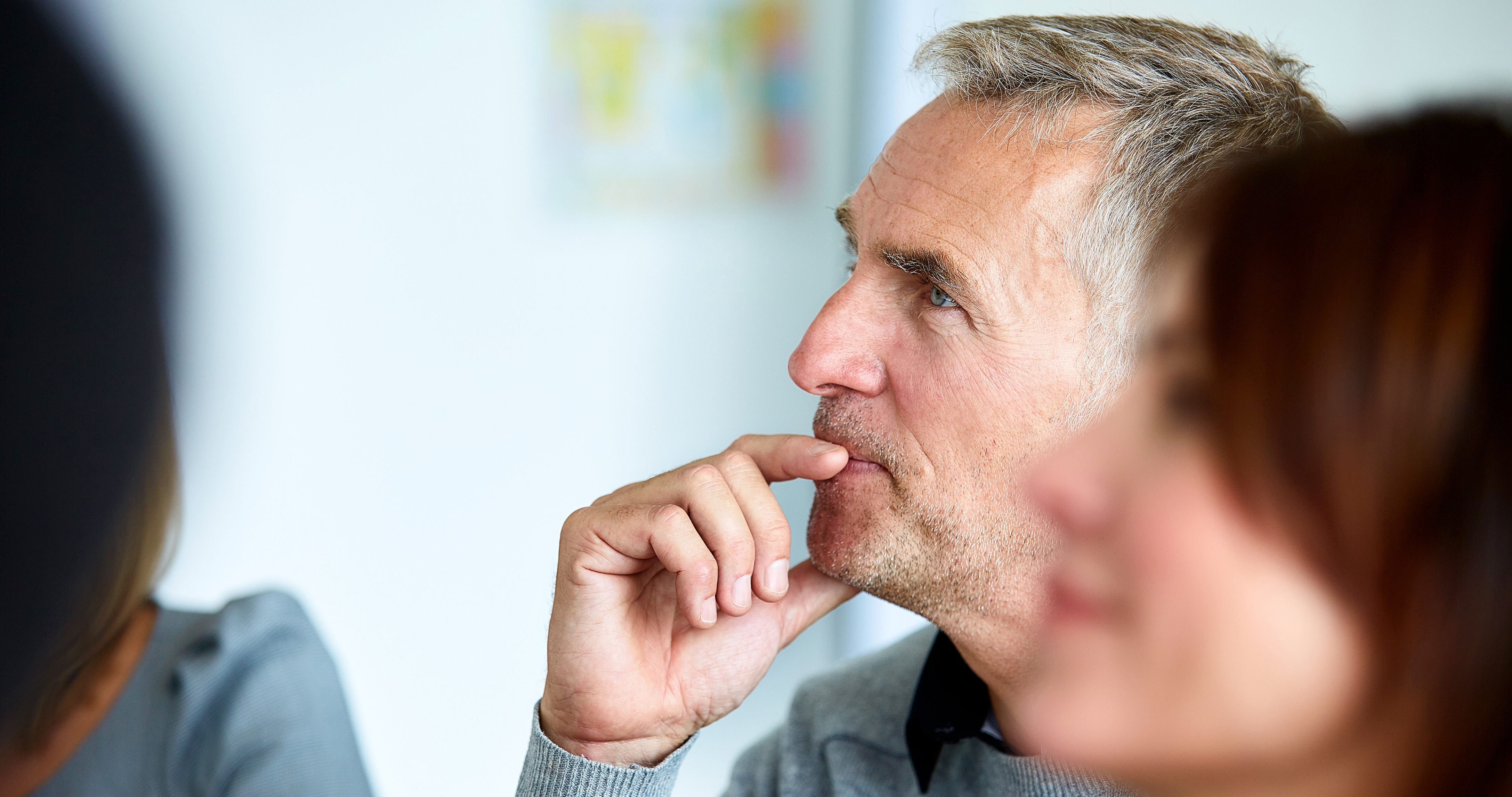 A man sitting in a leadership essentials session, thoughtfully listening to the trainer with his hand on his mouth.