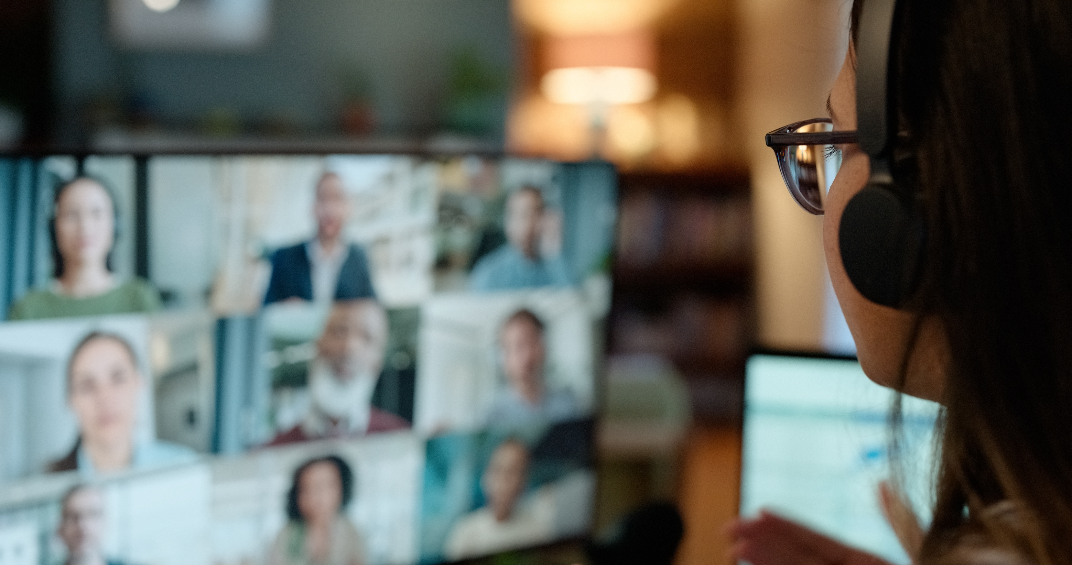 A woman engaged in a Learning Leaders Network remote call, wearing earphones and participating in a virtual room with a large group of people.