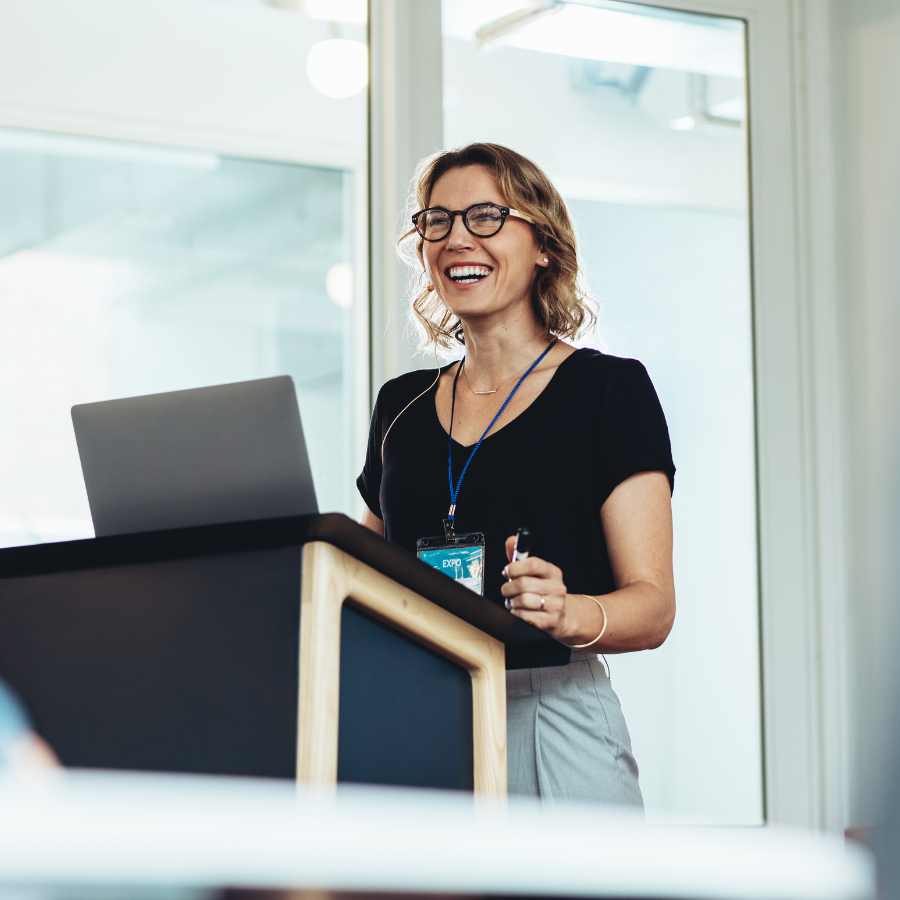 A woman presenting a leadership development session, smiling and engaging with the audience in a room
