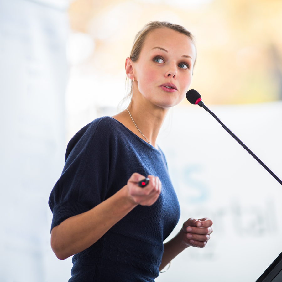 A woman preparing to present in a High Performer Programme, speaking to the audience while holding a clicker in her hand.