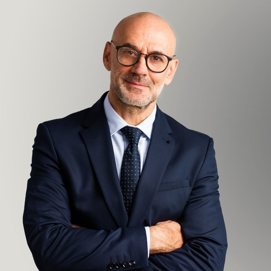 An executive leader, a man with arms crossed, smiling and looking into the camera with an inviting demeanor.