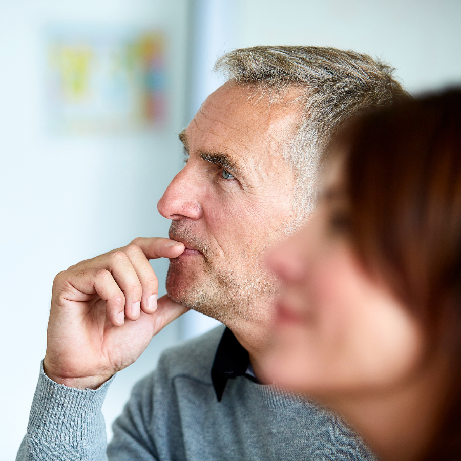 A man sitting in a leadership essentials session, thoughtfully listening to the trainer with his hand on his mouth.